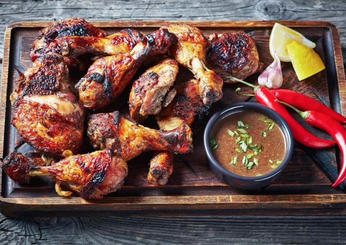 Jerk chicken on chopping board with sauce and chillies