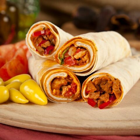 Turkish Tantuni wraps served with colored peppers on a wooden cutting board.