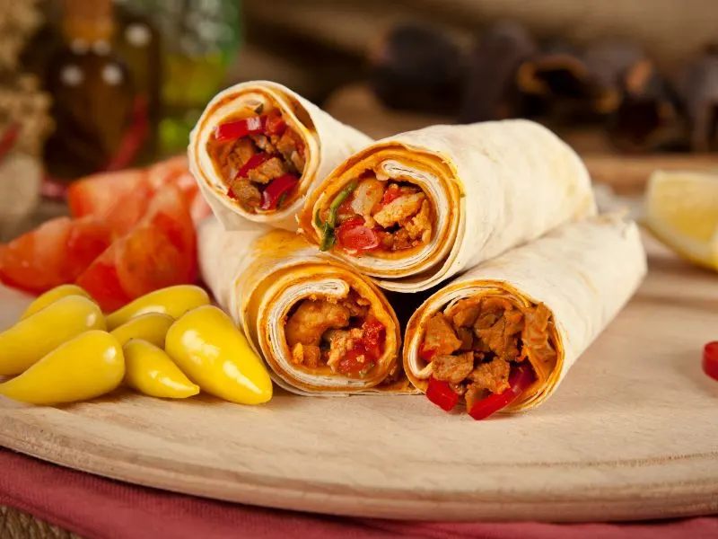 Turkish Tantuni wraps served with colored peppers on a wooden cutting board.