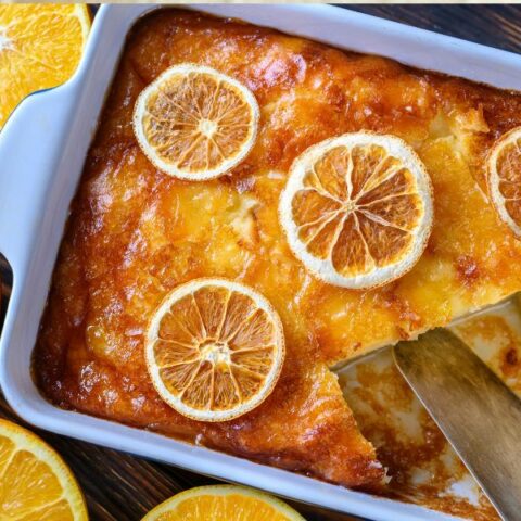 Portokalopita cake in a tin with oranges on top
