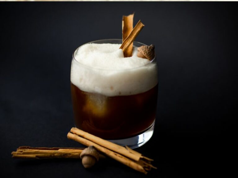 Coffee cocktail with foam and cinnamon sticks against a dark back ground.