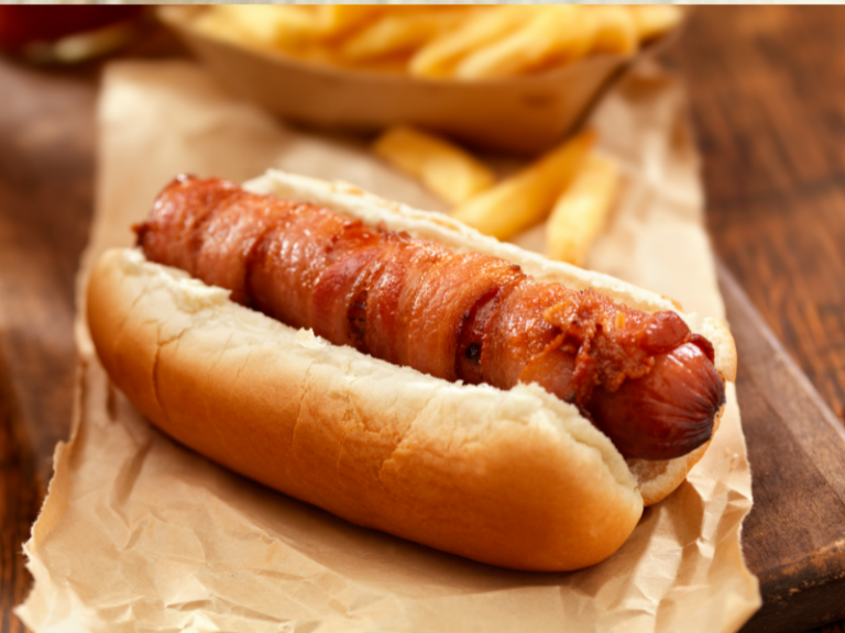 Hot dog wrapped in bacon in a bun on a paper bag