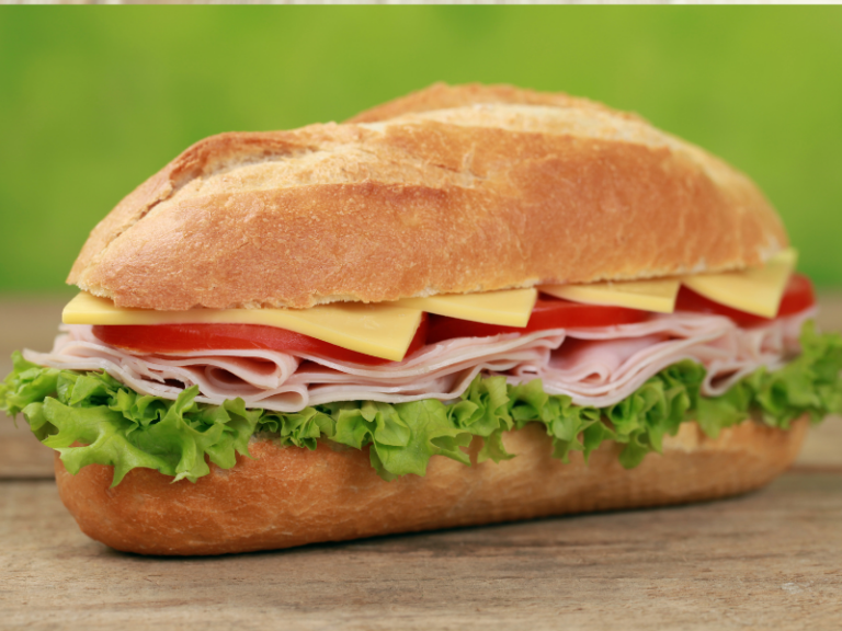 bread roll with ham, cheese, tomato and salad on a wooden board