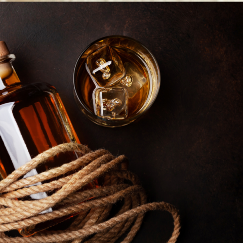 Bottle of rum wrapped in rope with a glass of rum and ice next to it