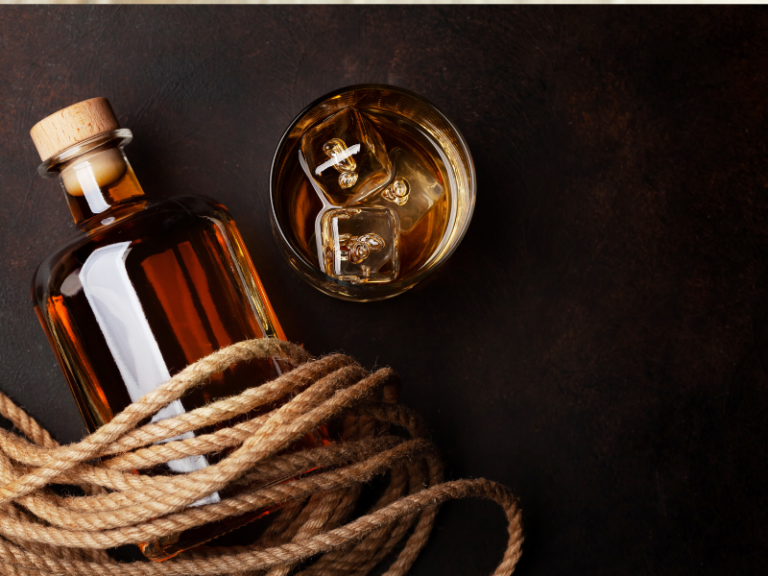 Bottle of rum wrapped in rope with a glass of rum and ice next to it