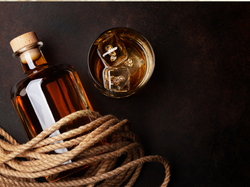 Bottle of rum wrapped in rope with a glass of rum and ice next to it