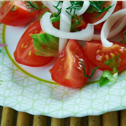 Tomatoes and onions on a white plate with dressing and herbs