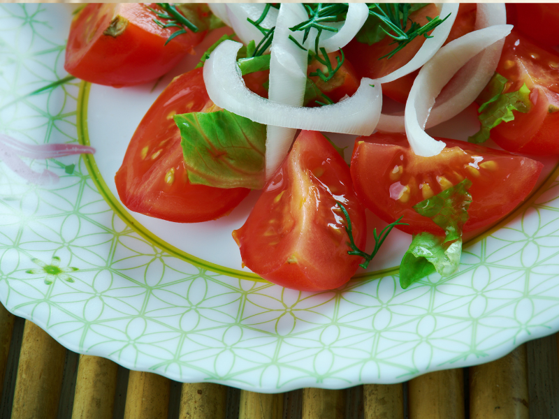 Tomatoes and onions on a white plate with dressing and herbs