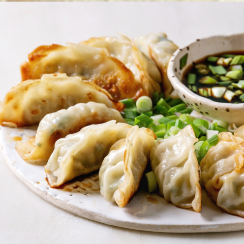 Dumplings on a plate with spring onions and a bowl of dipping sauce