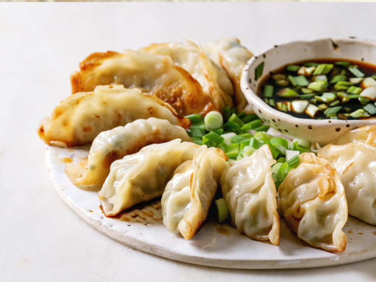 Dumplings on a plate with spring onions and a bowl of dipping sauce