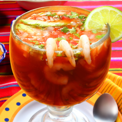 Large glass of seafood cocktail in a red liquid with shrimp and lime on the rim of the glass
