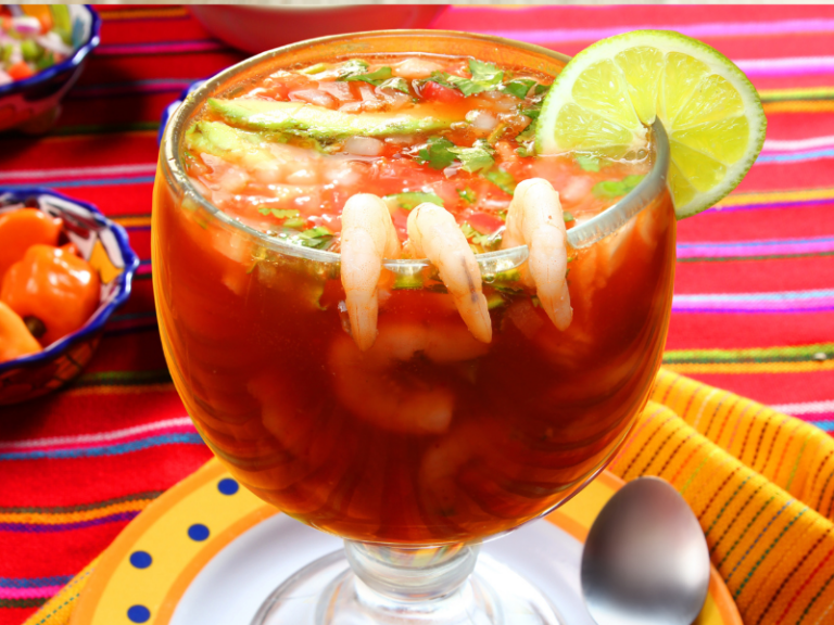 Large glass of seafood cocktail in a red liquid with shrimp and lime on the rim of the glass