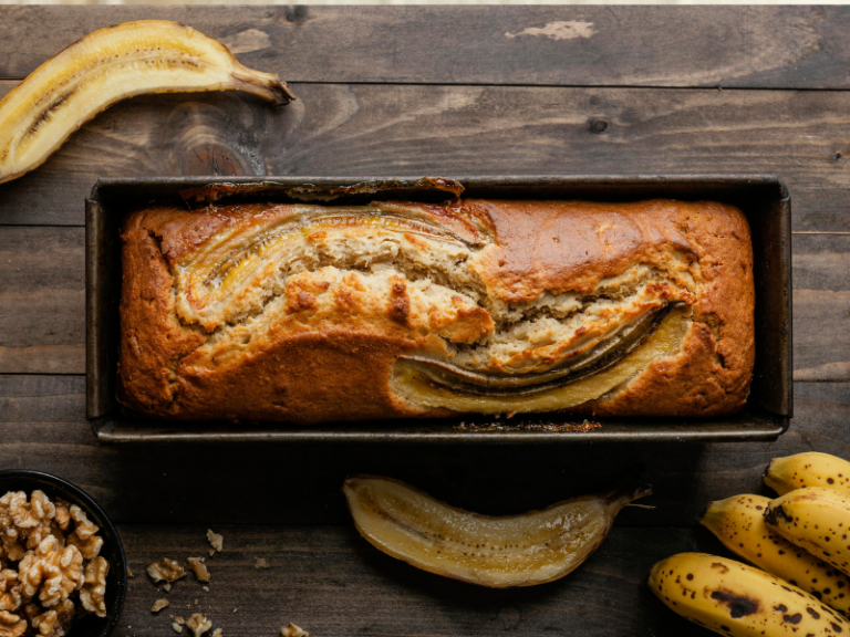 Banana cake in a tin, on a wooden bench with bananas on the bench.