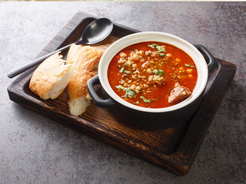 Bowl of soup on a black plate with bread on the side