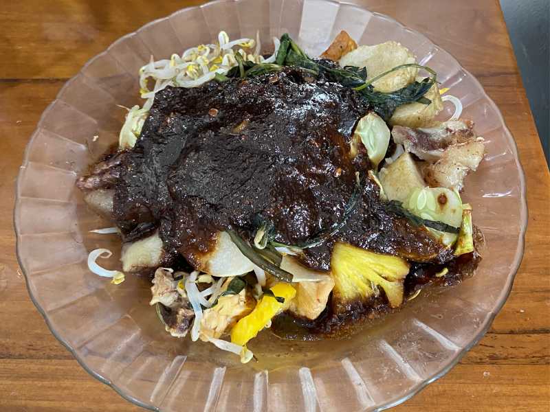 Rujak Cingur with pineapples and dark sauce.
